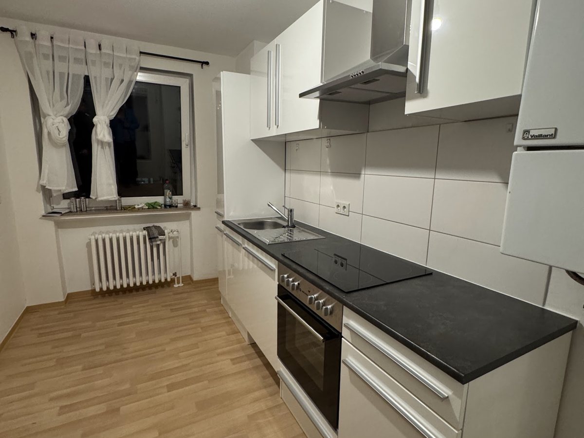 Weiße Küche mit dunkler Arbeitsplatte an einer Fensterwand